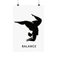 A minimalist black and white poster featuring a silhouette of a gymnast performing a handstand with the word 'BALANCE' printed below, shown hanging from two black clips against a white background.