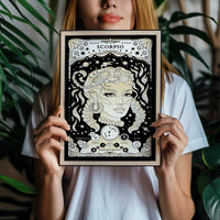 woman holds frame with Scorpio cosmic zodiac portrait featuring a feminine figure surrounded by a scorpion, stars, planets, Scorpio constellation, Mars and Pluto symbols, and Water element