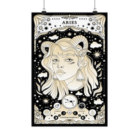 A vertical Aries zodiac poster with an illustrated ram-horned woman, stars, clouds, and celestial details in cream and black, hanging from two black clips against a light gray background.