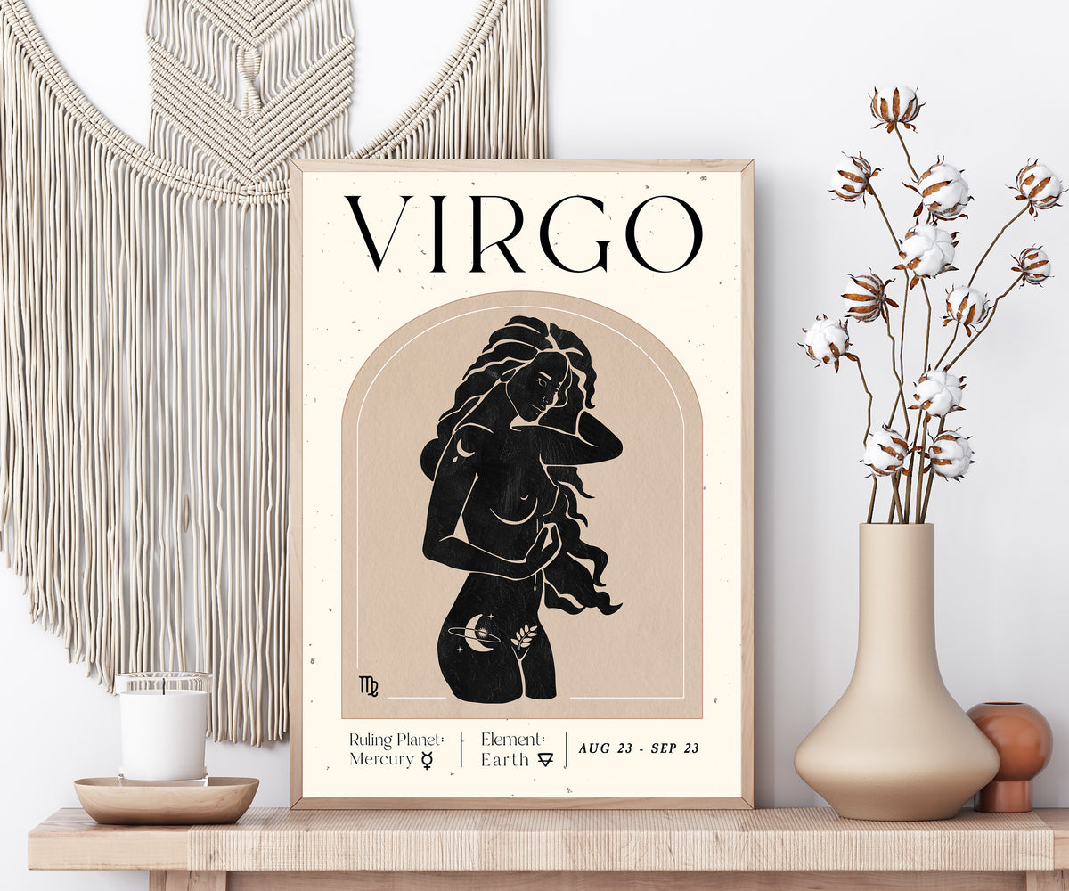 A framed Virgo astrology art print styled on a wooden shelf next to a macrame wall hanging, a candle, and a vase with dried cotton stems.