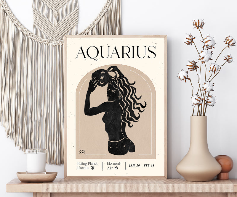 A framed art print featuring a retro Aquarius zodiac poster with a black silhouette of a woman and cream text on a beige background, styled on a wooden shelf with a macrame wall hanging, a candle, and a vase with dried flowers.