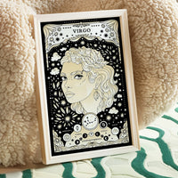 poster leaning against chair Virgo cosmic zodiac portrait featuring a feminine figure surrounded by botanical details, stars, Virgo constellation, Mercury symbol, and Earth element
