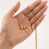 A gold box chain necklace with a '444' numerals pendant is held in a person's hand against a clean white background.