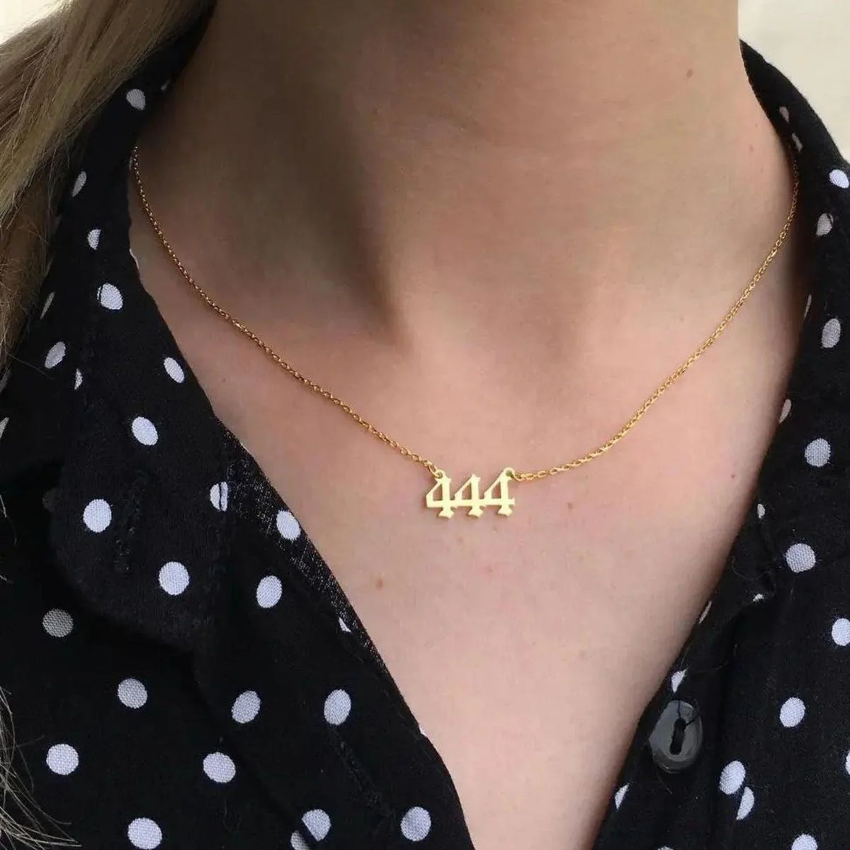 Gold 444 angel number necklace on woman's neck, spiritual jewelry, black polka dot shirt