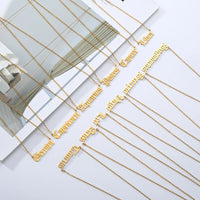 A set of gold necklaces with gothic script zodiac signs laid out on a white surface with a magazine page underneath, 
