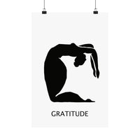 A minimalist poster print featuring a black silhouette of a person in a gratitude pose on a white background, with the word 'GRATITUDE' printed below. The poster is shown hanging from two black clips against a white background.