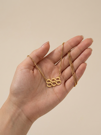 A gold box chain necklace with a angel number 888, held in a person's hand against a soft beige background.