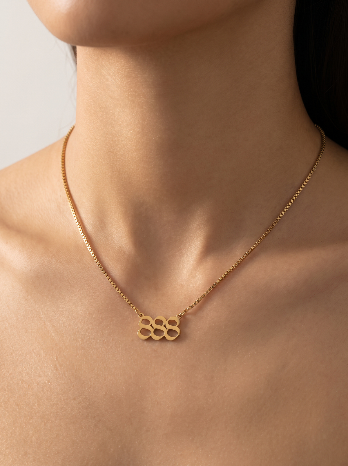A close-up of a model's neck and upper chest wearing a delicate gold chain necklace with a angel number 888