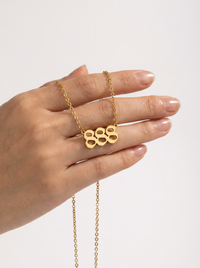 A gold necklace with an angel number 888 pendant , held on a person's fingers against a clean, light gray background.