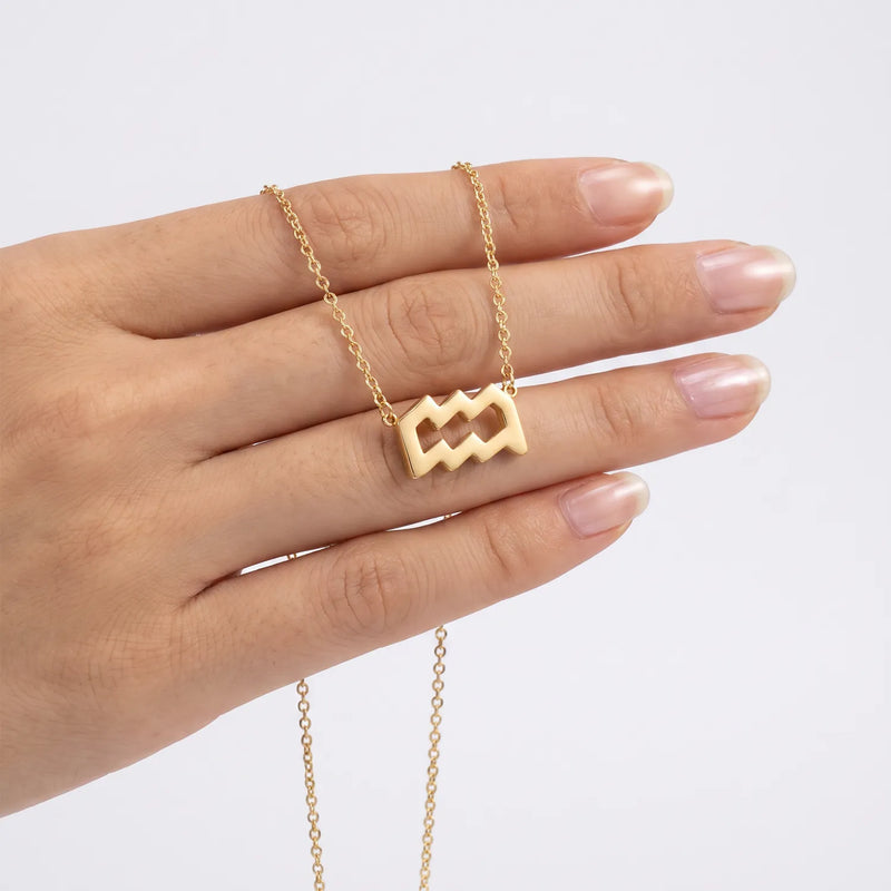 A gold necklace with an aquarius pendant is draped over a person's hand against a clean white background