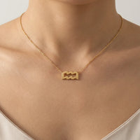 A close-up of a model's neck and upper chest wearing a delicate gold chain necklace with an aquarius sign pendant