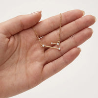 A delicate gold necklace with a aries constellation pendant, held in the palm of a hand against a clean white background.