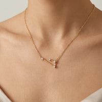 A delicate gold necklace with a aries constellation pendant featuring small clear gemstones, shown worn on a model's neck.
