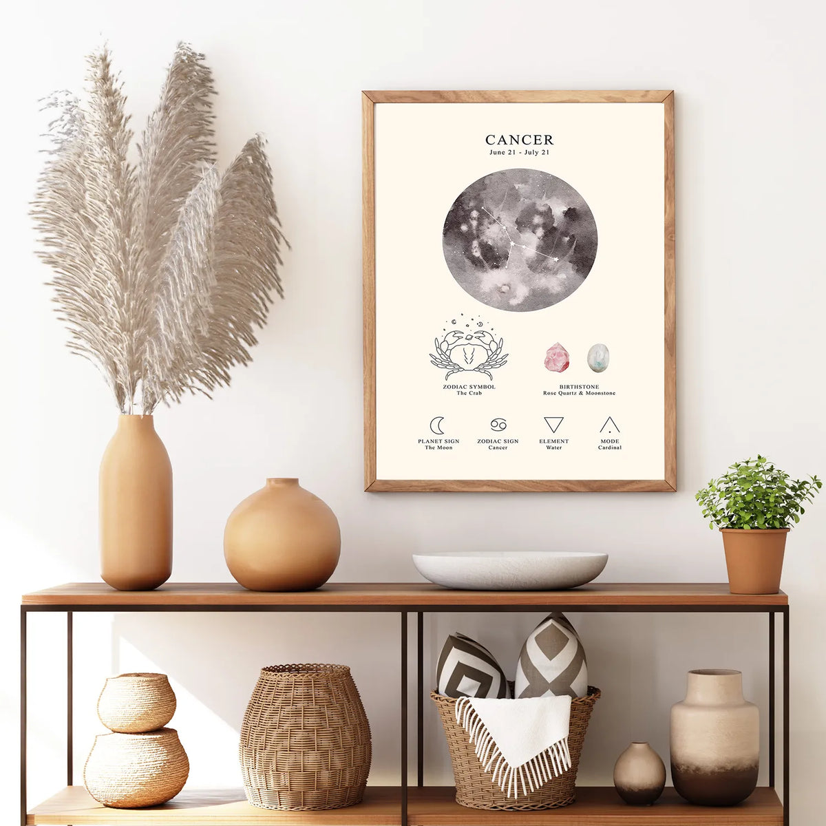A framed astrology poster for Cancer featuring a detailed moon illustration and astrological symbols, styled on a wooden console table with decorative vases, a bowl, and a potted plant in a bright room.