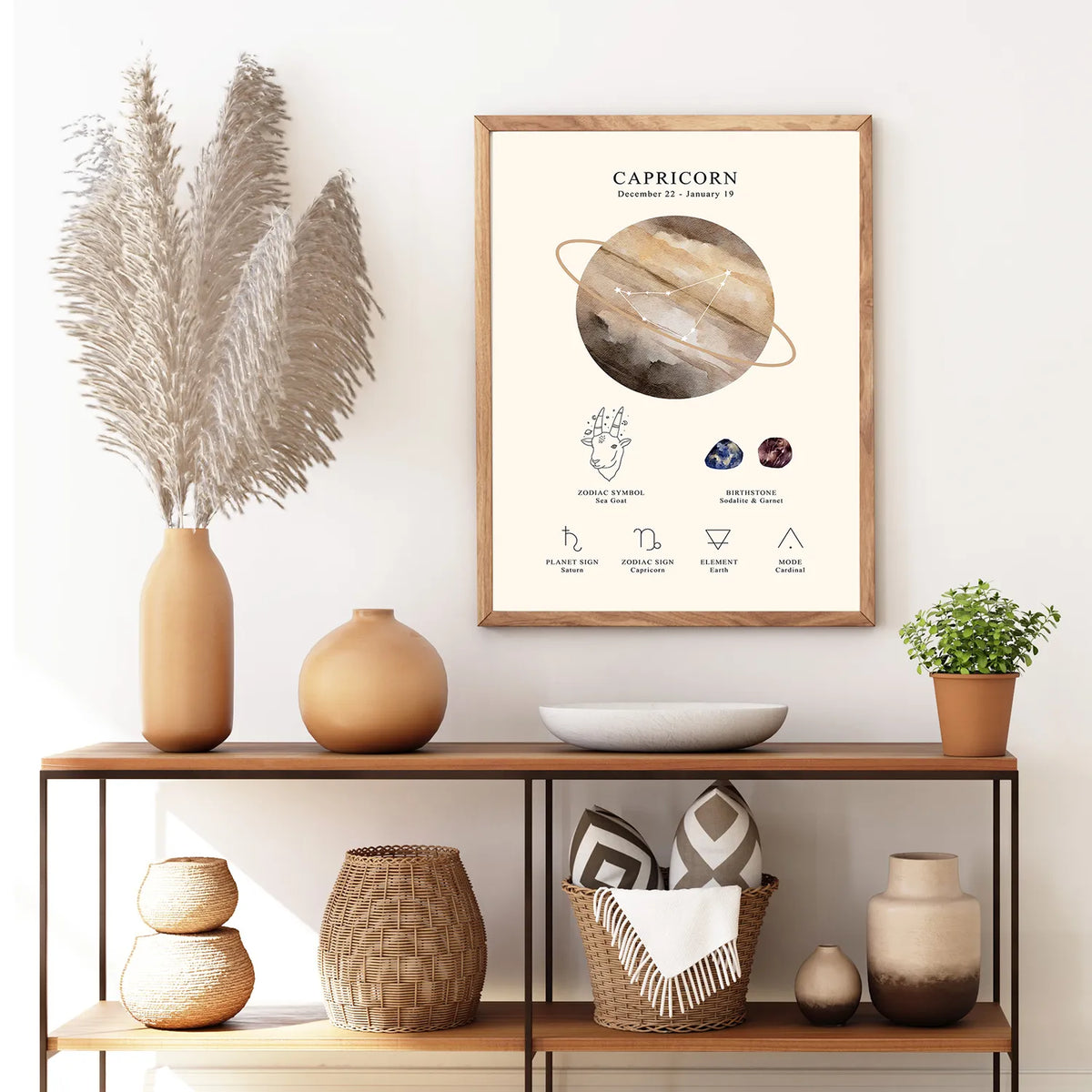 A framed Capricorn zodiac poster hangs on a white wall above a wooden console table styled with vases, a pampas grass arrangement, a bowl, and a small plant.