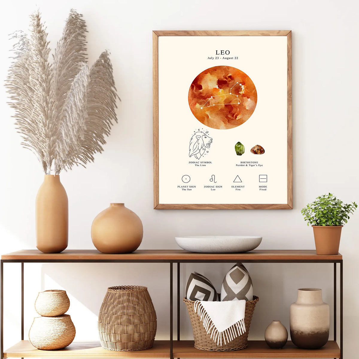A framed Leo zodiac art print hangs on a white wall above a wooden console shelf styled with vases, a bowl, a basket, and a small potted plant. The print features a watercolor orange Leo sun and constellation details on an off-white background.