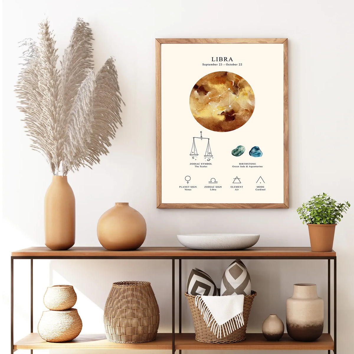 A framed Libra astrology poster hangs on a white wall above a wooden console table styled with vases, a plant, and woven decor. The poster features a gold-toned Libra sun graphic and astrological details.