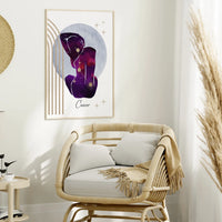 A framed art print featuring a purple Cancer zodiac symbol with gold stars and lines, displayed on a white wall above a rattan armchair in a styled room.