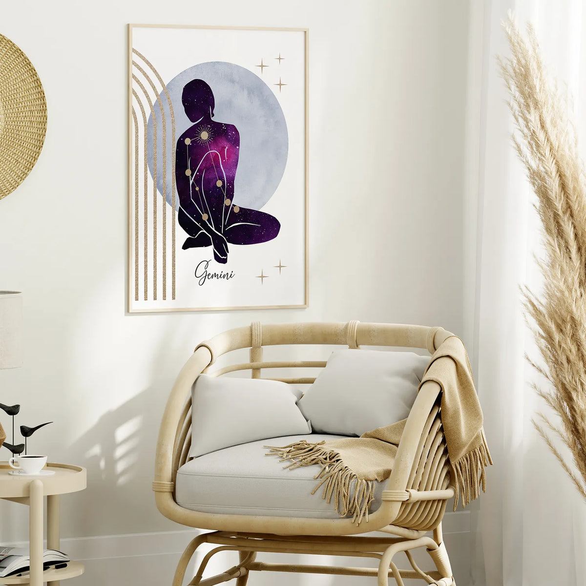 A framed art print featuring a Gemini zodiac sign illustration with a purple silhouette and gold stars, displayed on a white wall above a rattan armchair in a styled room.
