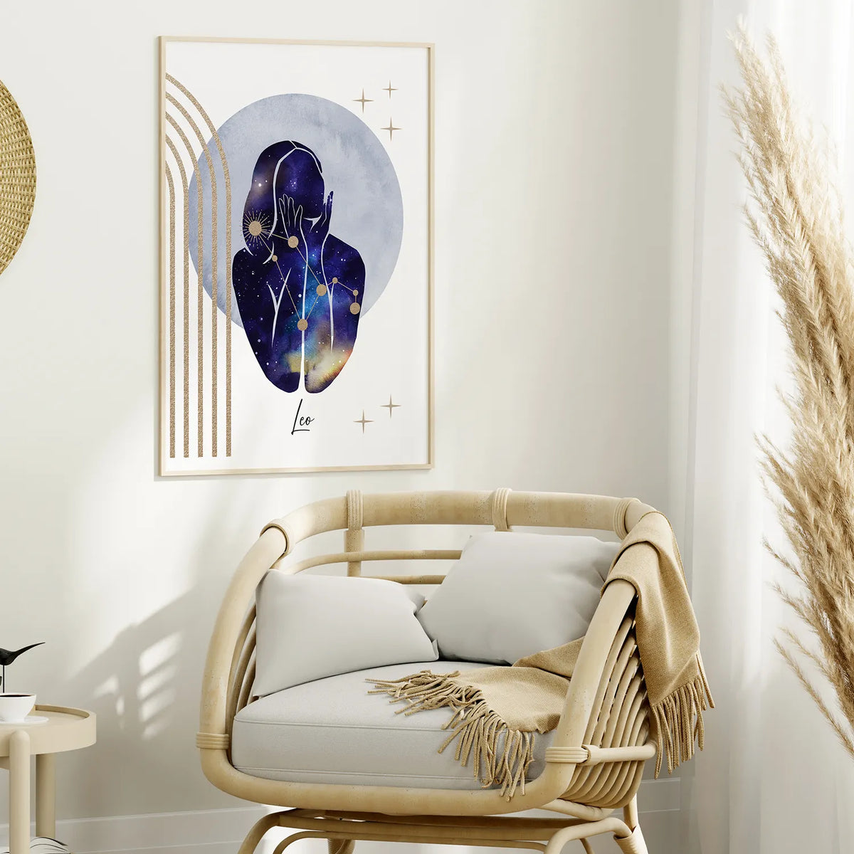 A framed wall art print hangs above a light wood rattan armchair in a styled interior. The artwork shows an abstract human silhouette filled with a galaxy-like blue, purple, and gold pattern on a white background with gold geometric lines.