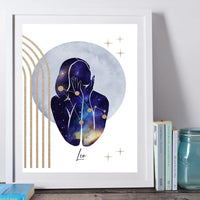 A framed art print featuring a stylized silhouette of a person in a galaxy pattern, set against a large blue-gray circle with gold stars and arches, displayed on a shelf next to books and a mason jar.