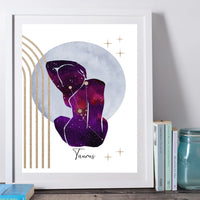 A framed art print featuring a purple and pink galaxy-style Taurus zodiac sign silhouette, gold arches and stars, and the word 'Taurus' at the bottom, displayed leaning against a wall beside books and a glass jar.