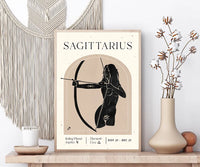 A framed Sagittarius astrology poster displayed on a wooden shelf in a styled room setting, flanked by a beige macrame wall hanging, a lit candle, and a ceramic vase with dried cotton stems.