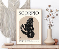 A framed Scorpio zodiac art print displayed on a wooden shelf, styled with a macrame wall hanging, a candle, cotton stems in a vase, and decorative spheres against a white wall.
