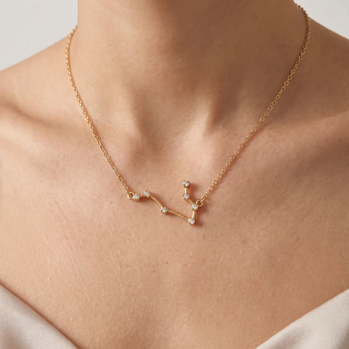 A delicate gold necklace with a constellations-inspired crystal pendant, shown worn on a model's neck. The pendant features small clear gemstones set in gold 