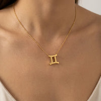 A gold necklace with a Gemini zodiac symbol pendant, worn on a model's neck.