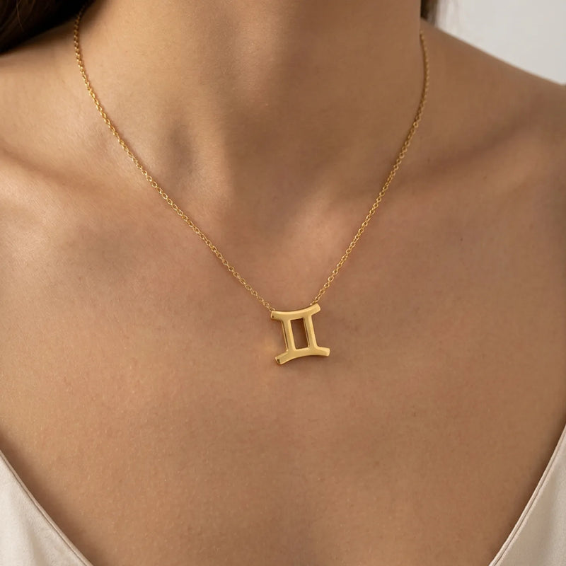 A gold necklace with a Gemini zodiac symbol pendant, worn on a model's neck.