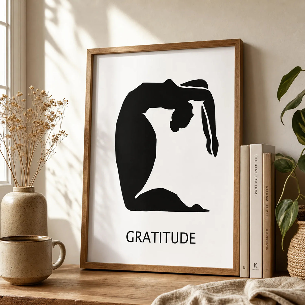 A minimalist black graphic print featuring a silhouette of a person in a graceful arching pose, with the word 'GRATITUDE' and a brown frame