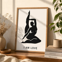 A minimalist black graphic print featuring a silhouette of a woman in a yoga pose with her leg raised, above the text 'I AM LOVE'  in a brown frame