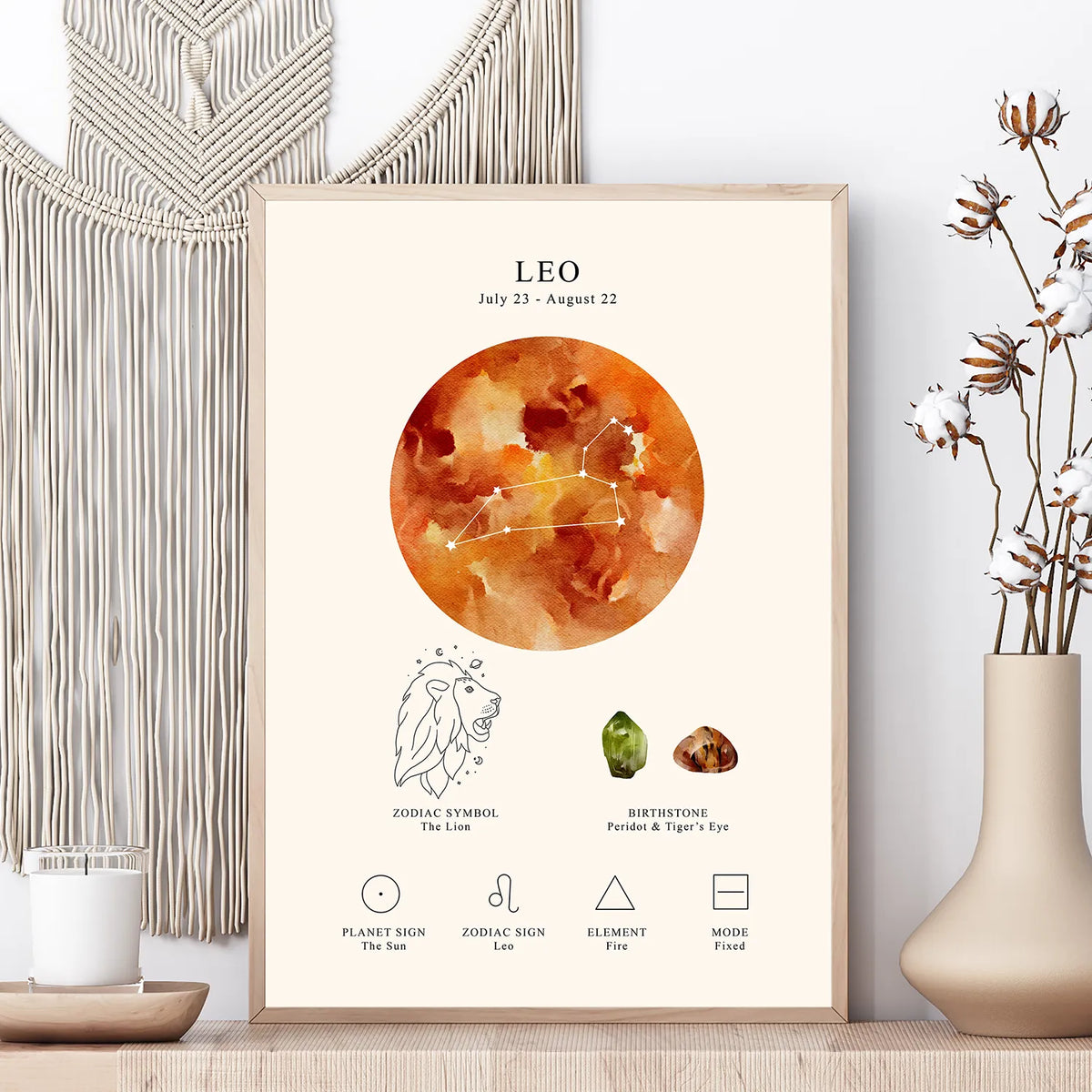 A framed astrology art print for Leo, styled on a wooden surface with a macrame wall hanging, a candle, and a vase in the background.