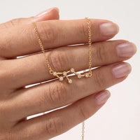 A gold necklace with a Leo constellation pendant is shown resting on a person's hand against a clean white background.