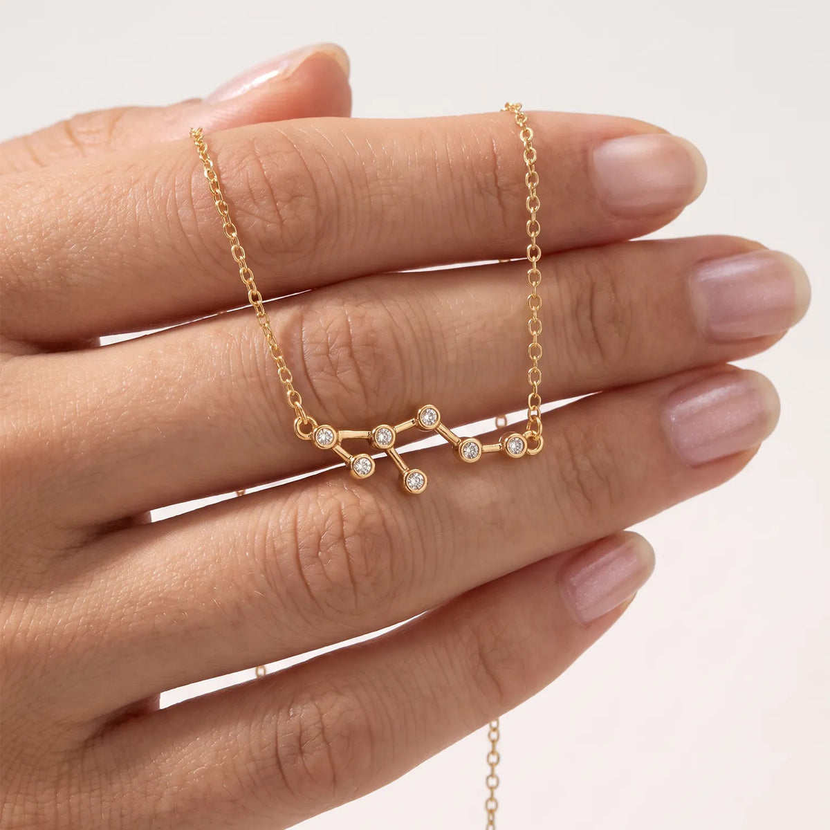 A gold necklace with a Leo constellation pendant is shown resting on a person's hand against a clean white background.