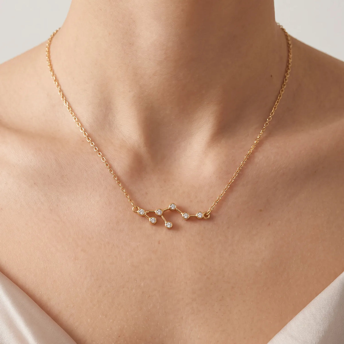 A delicate gold chain necklace with a leo constellation pendant set with clear gemstones, shown worn on a model's neck.
