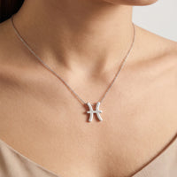 A close-up of a person's neck and chest wearing a delicate gold chain necklace with a pisces zodiac sign pendant