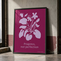 Framed botanical art print featuring lavender flowers on a rich berry-pink background with the words “Progress, not perfection.” w black frame