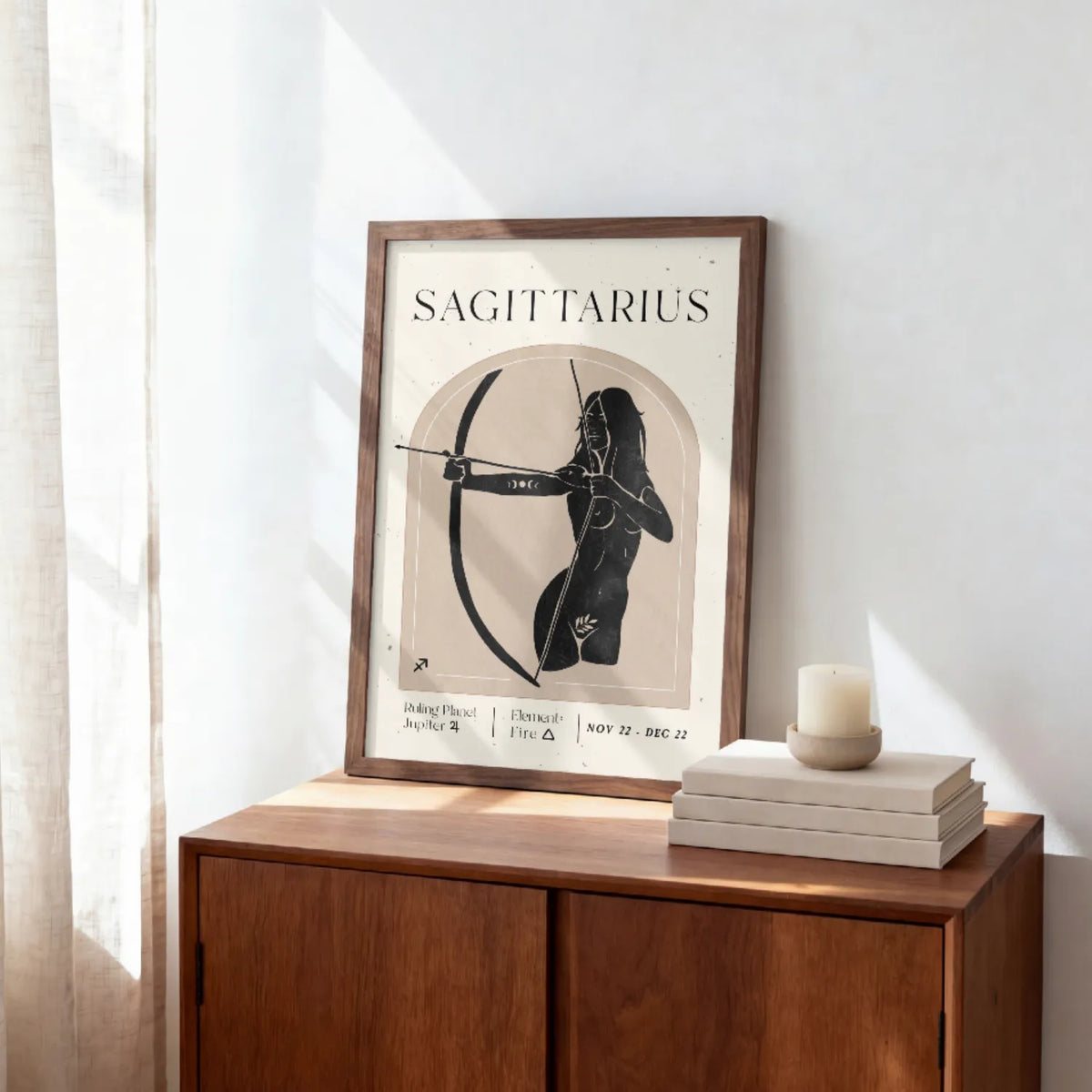 A framed Sagittarius poster with a black and beige illustration of a bowhunter, styled on a wooden sideboard next to a candle and books in a sunlit room.