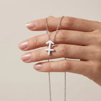 A golden necklace with a Sagittarius zodiac symbol pendant held by a hand against a solid beige background.