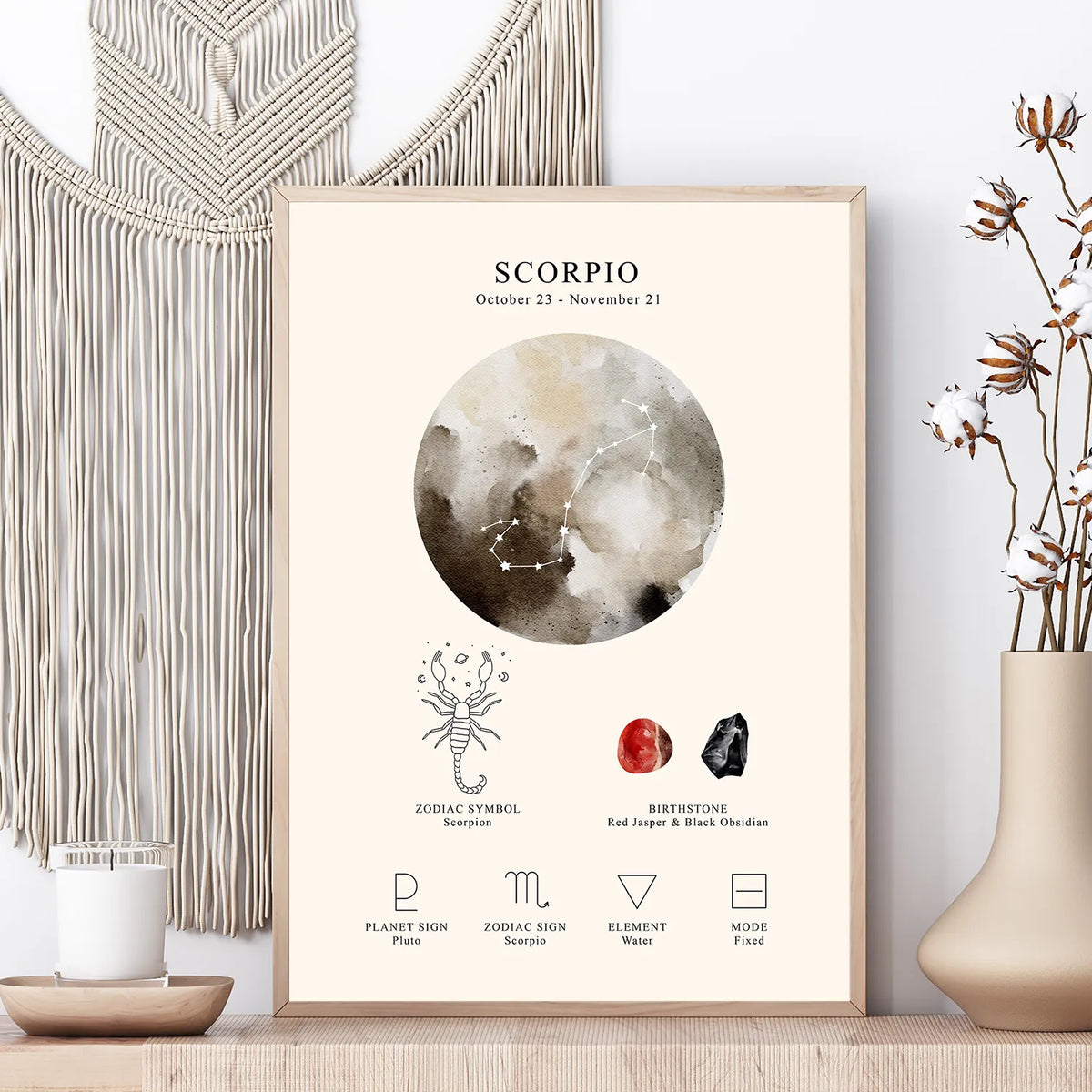 A framed Scorpio zodiac art print displayed on a wooden surface, styled with a macrame wall hanging, a candle, and dried flowers in a vase.