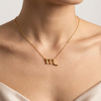 A close-up of a model's neck and chest wearing a delicate gold chain necklace with a zodiac sign Scorpio pendant.