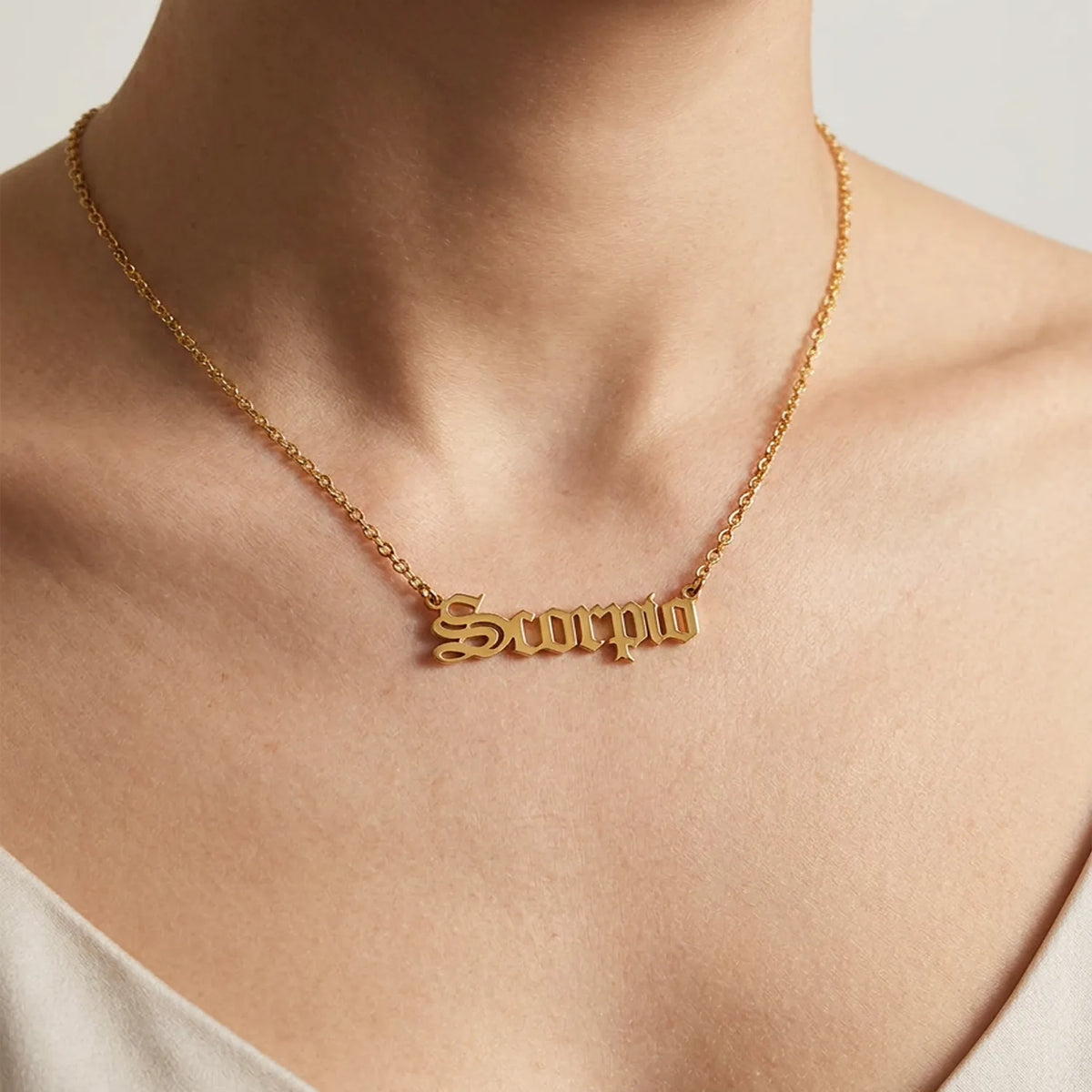 A gold nameplate necklace spelling scorpio in a scripted font worn on a model's neck, shown in a close-up 