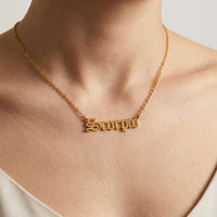 A gold nameplate necklace spelling scorpio in a scripted font worn on a model's neck, shown in a close-up 