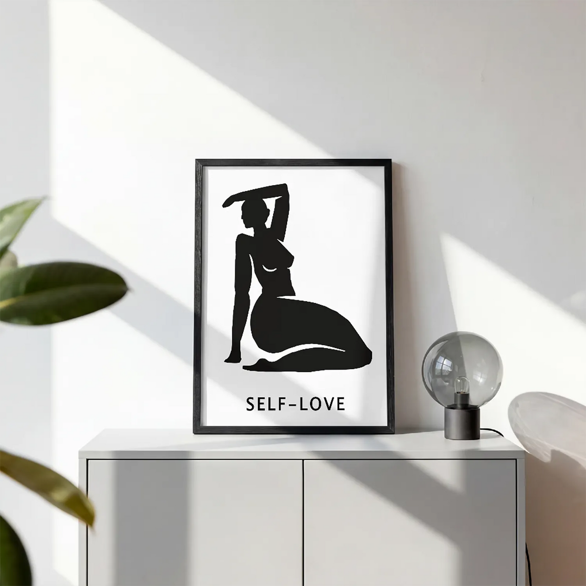 A minimalist black graphic print featuring a silhouette of a kneeling woman with one arm raised, above the text 'SELF-LOVE'  with black frame