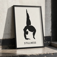 A minimalist wall art print featuring a black silhouette of a person in a handstand pose on a white background, with the word 'STILLNESS' in black frame