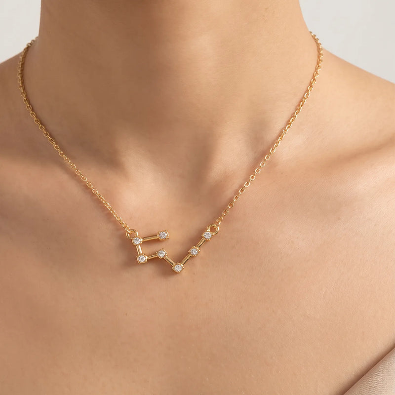 A gold necklace with a taurus constellation pendant featuring small clear gemstones, shown worn on a model's neck and upper chest.