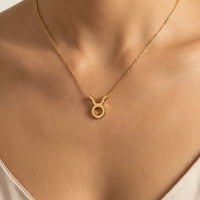 A gold necklace with a  taurus zodiac sign pendant, displayed on a models neck