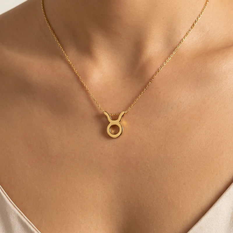 A gold necklace with a  taurus zodiac sign pendant, displayed on a models neck